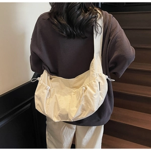 Detail of a large beige crescent bag showing drawstring pleats and wide shoulder strap