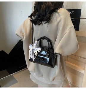 Detail of glossy black bow handbag with blue checkered ribbon on the handle