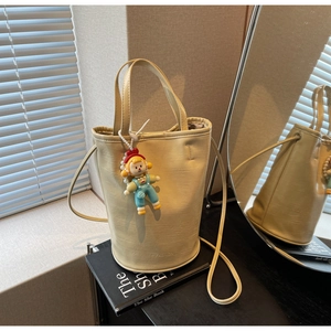 Detail of cream yellow leather bucket bag with fashion embossing and cartoon charm decoration