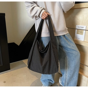 Detail of large canvas tote bag with dark checkered pattern worn on shoulder for commuting