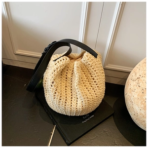 Close-up of cream woven bucket bag texture with contrast black leather strap detail