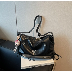 Detail of black pleated crossbody bag with silver butterfly accents and bear charm