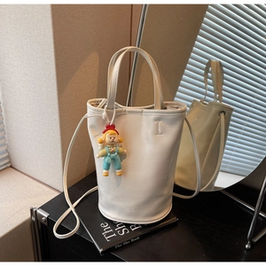 Detail of white leather bucket bag with FASHION text and cute doll charm on black desk