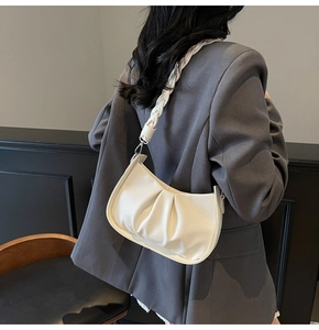 Close-up of white pleated crescent shoulder bag with braided strap and silver metal hardware