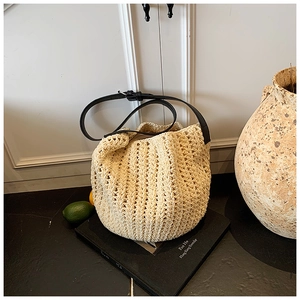 Detail view of cream woven bucket bag featuring thick hollow mesh and adjustable black strap