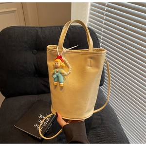 Detail of beige bucket bag featuring crocodile texture, pearl chain and clown charm