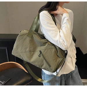 Detailed view of an olive green nylon travel bag shown on shoulder in indoor setting