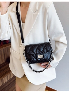 Quilted black crossbody bag with silver chain strap and metal turn-lock on white suit