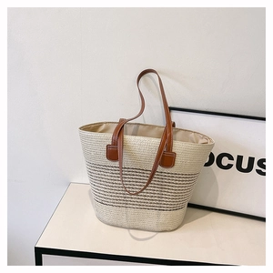 Dettaglio della borsa tote in paglia intrecciata con strisce marroni e manici