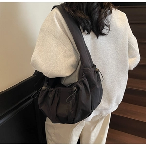 Side view of black nylon dumpling bag with drawstring and wide shoulder strap on model