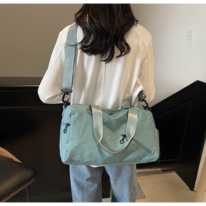 Rear view of a model carrying a large light blue waterproof nylon travel bag with shoulder strap