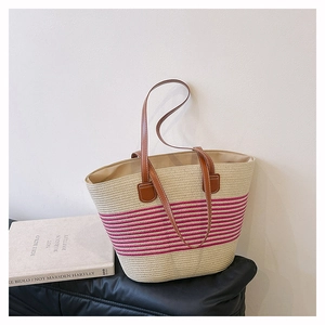 Dettaglio della borsa tote in paglia con strisce rosa e manici in pelle marrone su cuscino