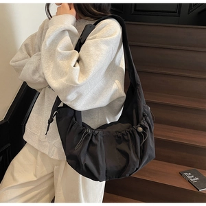 Close-up of black nylon dumpling bag featuring drawstring pleats and wide shoulder strap