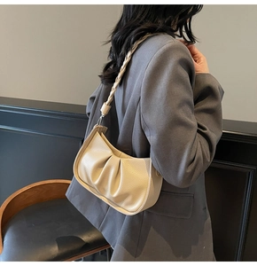 Close-up of litchi leather pleats and braided shoulder strap on beige underarm bag