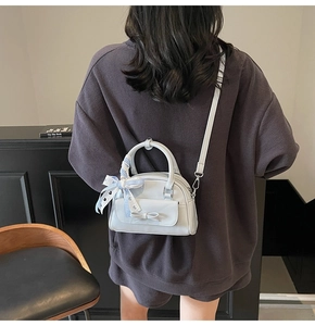 Light blue crossbody pillow bag with ribbon bow and dual zipper detail on a model