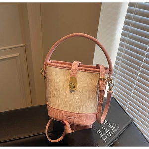 Détail d'un sac seau bicolore en cuir grainé avec fermoir métallique doré et texture lychee