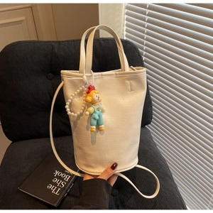 Detail of cream bucket bag featuring leather texture, pearl chain and cute clown charm