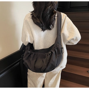 Detail of a black crossbody dumpling bag with drawstring side and nylon texture