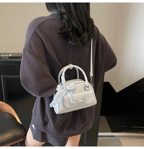 Detail showing a light blue Boston bag with a bow and plaid scarf on a crossbody strap