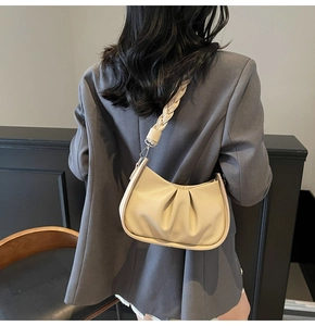 Detail of off-white pleated dumpling bag with thick braided strap on model's shoulder
