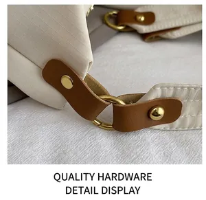 Detail of gold D-ring hardware and brown leather trim on a beige checkered tote bag