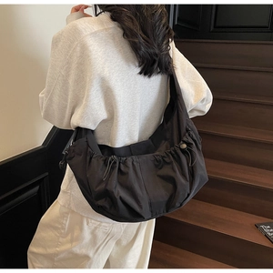 Detail of black dumpling shoulder bag showing side drawstring pleats and nylon texture