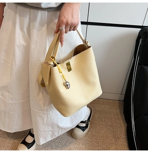 Detail of light yellow leather bucket bag featuring a gold clasp and heart pendant