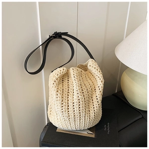 Detail of a beige woven bucket bag with black leather strap on a stylish book setting