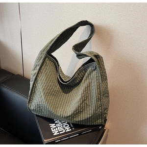 Detail of green checkered canvas tote bag showing textured fabric and wide strap on sofa
