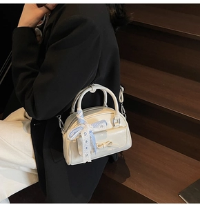 Detail of cream white boston bag with blue checkered ribbon on a model in black blazer