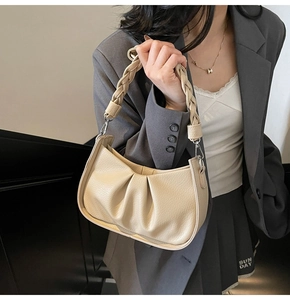 Detail of beige crescent underarm bag showing lychee leather texture and woven handle