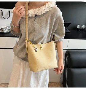 Detail of light yellow lychee grain leather bucket bag with gold lock and heart charm
