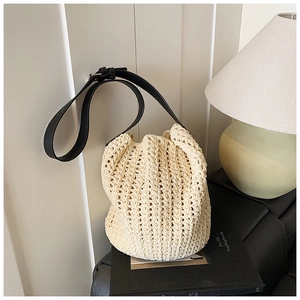 Detail of hand-woven beige bucket bag featuring a black leather strap on a sofa