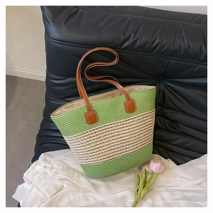 Dettaglio borsa tote in paglia intrecciata a righe verdi con manici in pelle sul divano