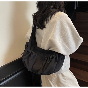 Model wearing black nylon dumpling bag with drawstring folds and adjustable strap detail