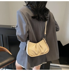 Detail of a beige crescent moon bag with pleated texture and silver hardware