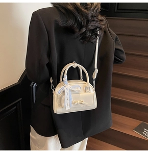 Creamy white crossbody bag with checkered ribbon handle shown on model in black blazer