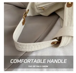 Detail of off-white tote bag handle with brown leather accents and gold hardware