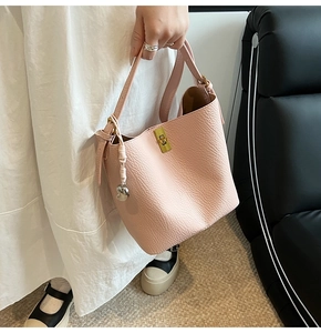 Pink lychee texture bucket bag with gold hardware and heart charm on a black sofa