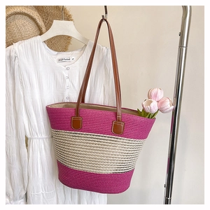 Dettaglio della borsa tote in paglia intrecciata a righe rosa con manici in pelle marrone