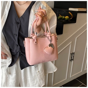 Detail of pink lychee leather bucket bag with heart pendant and knot handle detail