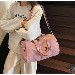 Pink multi-pocket travel bag with adjustable strap worn by model on stairs