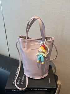 Lilac leather bucket bag with handle and charm over a black book in a lifestyle setting