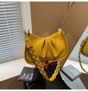 Detail of a bright yellow pleated leather handbag with a textured woven handle strap