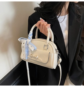 Detail of cream patent leather pillow bag with ribbon handle and bow accessory