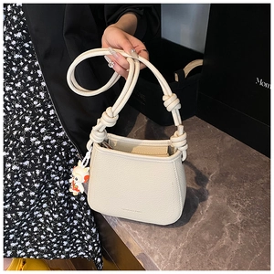 Detail of cream white pebbled leather bucket bag with knotted strap and cute doll charm