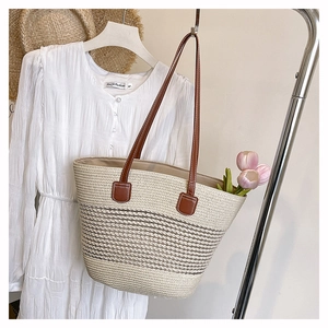 Dettaglio borsa tote in paglia intrecciata a righe con lunghi manici in ecopelle marrone