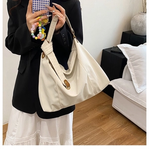 Detail of cream pleated tote bag featuring brown leather buckle and wide knotted strap