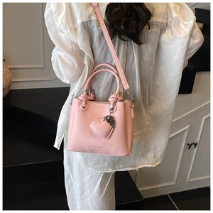 Pink bucket bag with heart charm and adjustable strap shown on model in white outfit
