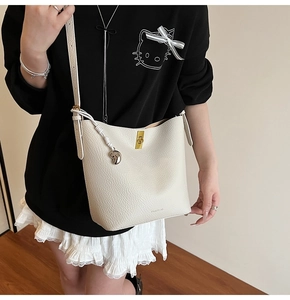 Detail of cream white leather bucket bag with gold twist lock and metallic charm on model
